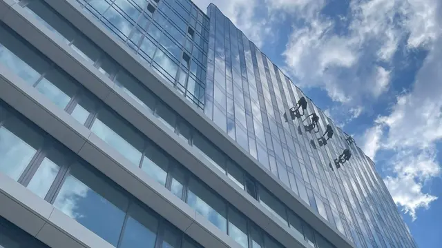 Skupina výškových pracovníků myje prosklenou fasádu pomocí lanové techniky